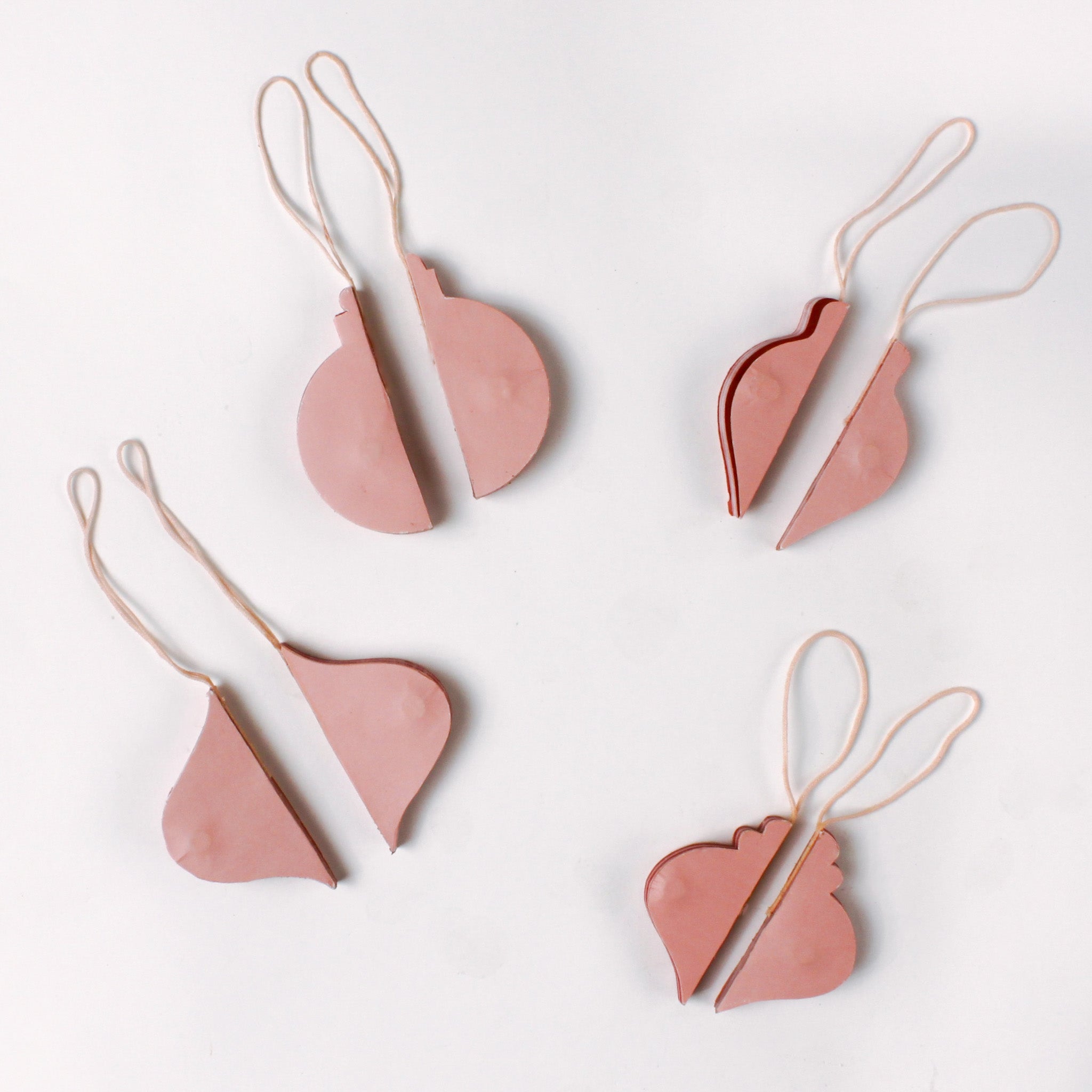 Set of folded flat pink paper Christmas ornaments in assorted bulb shapes with hanging strings, shown partially opened and ready for assembly.