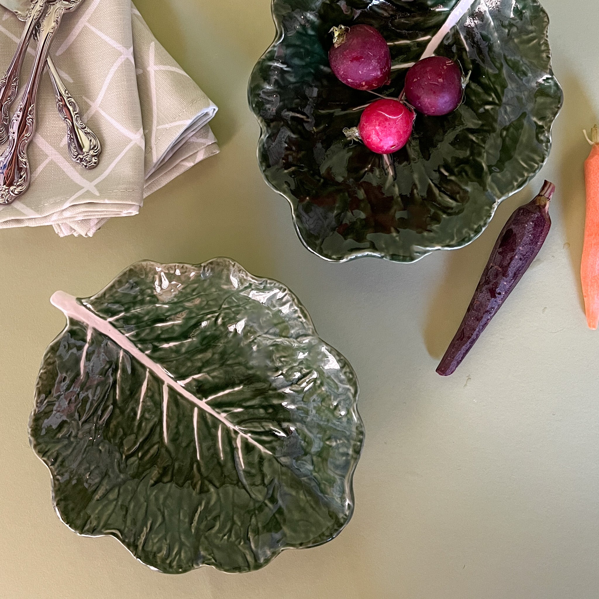 two ceramic cabbage leaf bowls one filled with radishes.