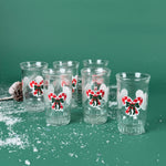 Set of six clear holiday tumblers with red candy cane bow designs on a snowy green background