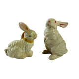 A pair of white vintage ceramic bunnies one with a yellow ribbon on its neck.
