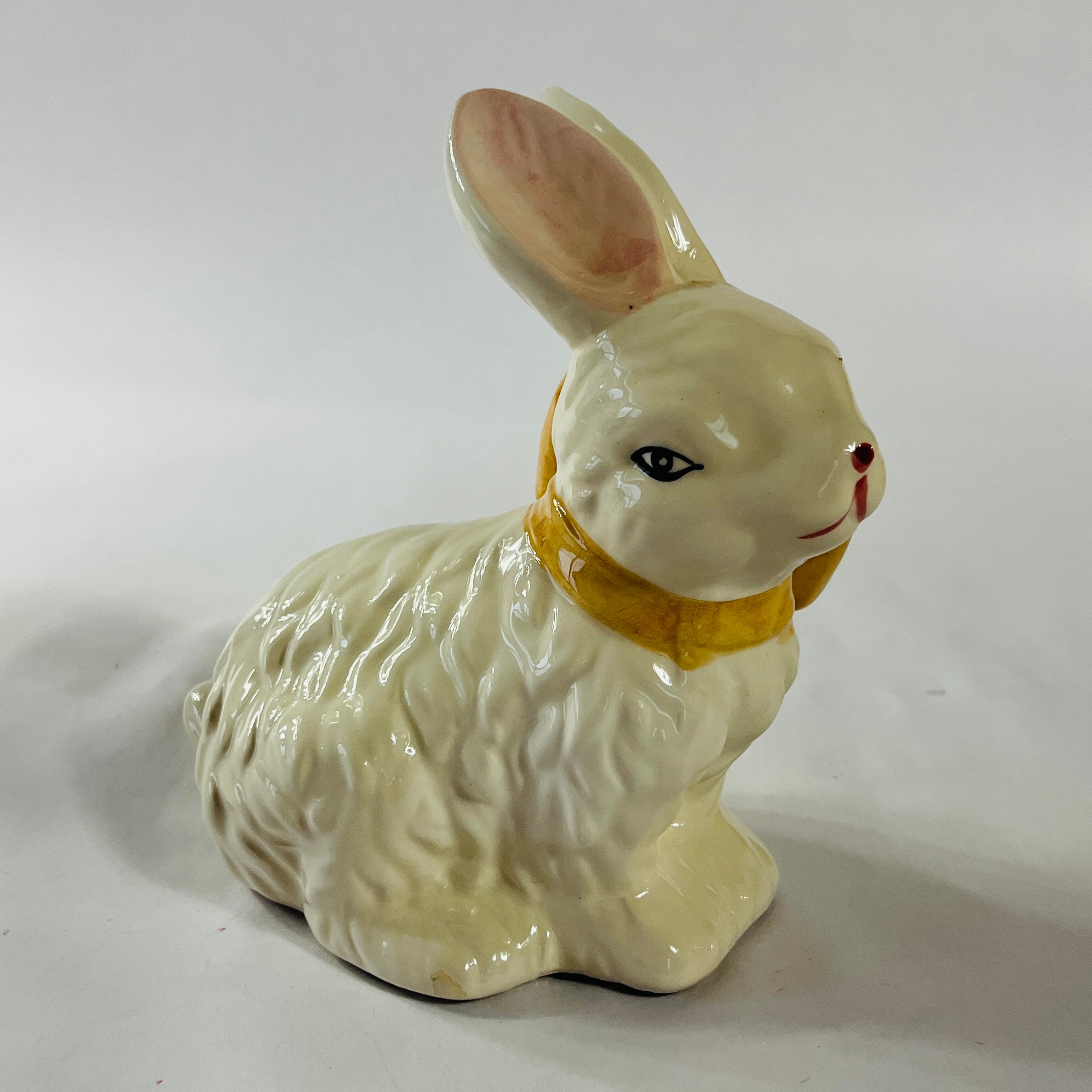 A white vintage ceramic bunnies one with a yellow ribbon on its neck.