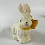 A white vintage ceramic bunnies one with a yellow ribbon on its neck.