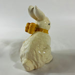 A white vintage ceramic bunnies one with a yellow ribbon on its neck.
