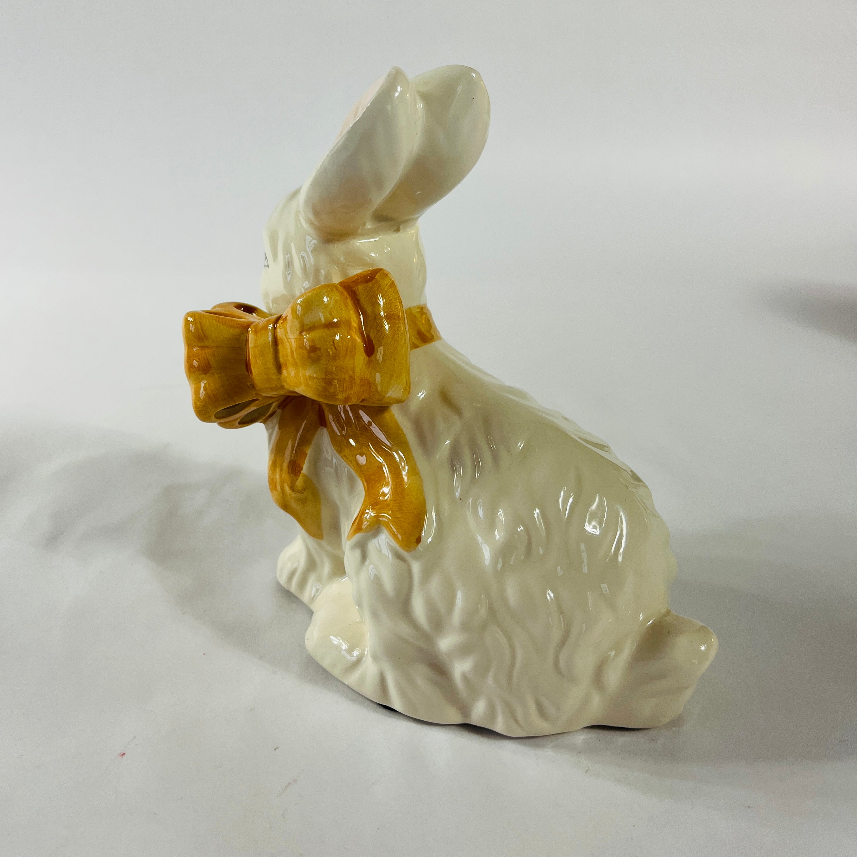 A white vintage ceramic bunnies one with a yellow ribbon on its neck.