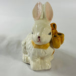 A white vintage ceramic bunnies one with a yellow ribbon on its neck.