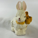A white vintage ceramic bunnies one with a yellow ribbon on its neck.