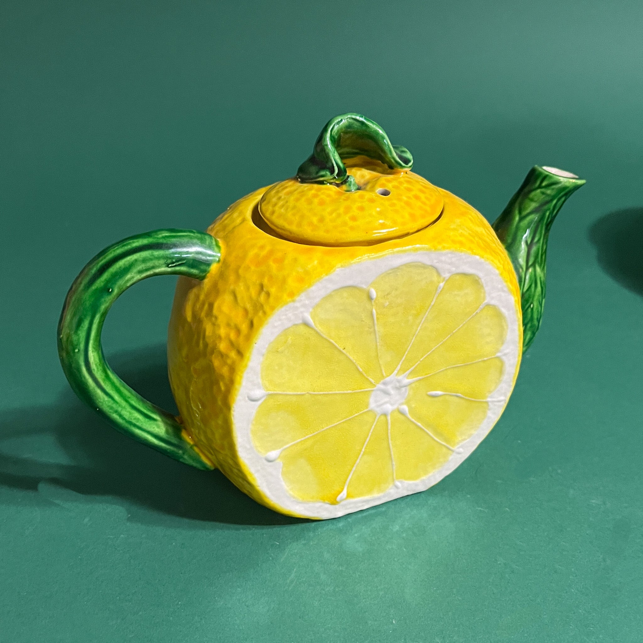 a lemon tea pot with a green spout and handle on a green background. 