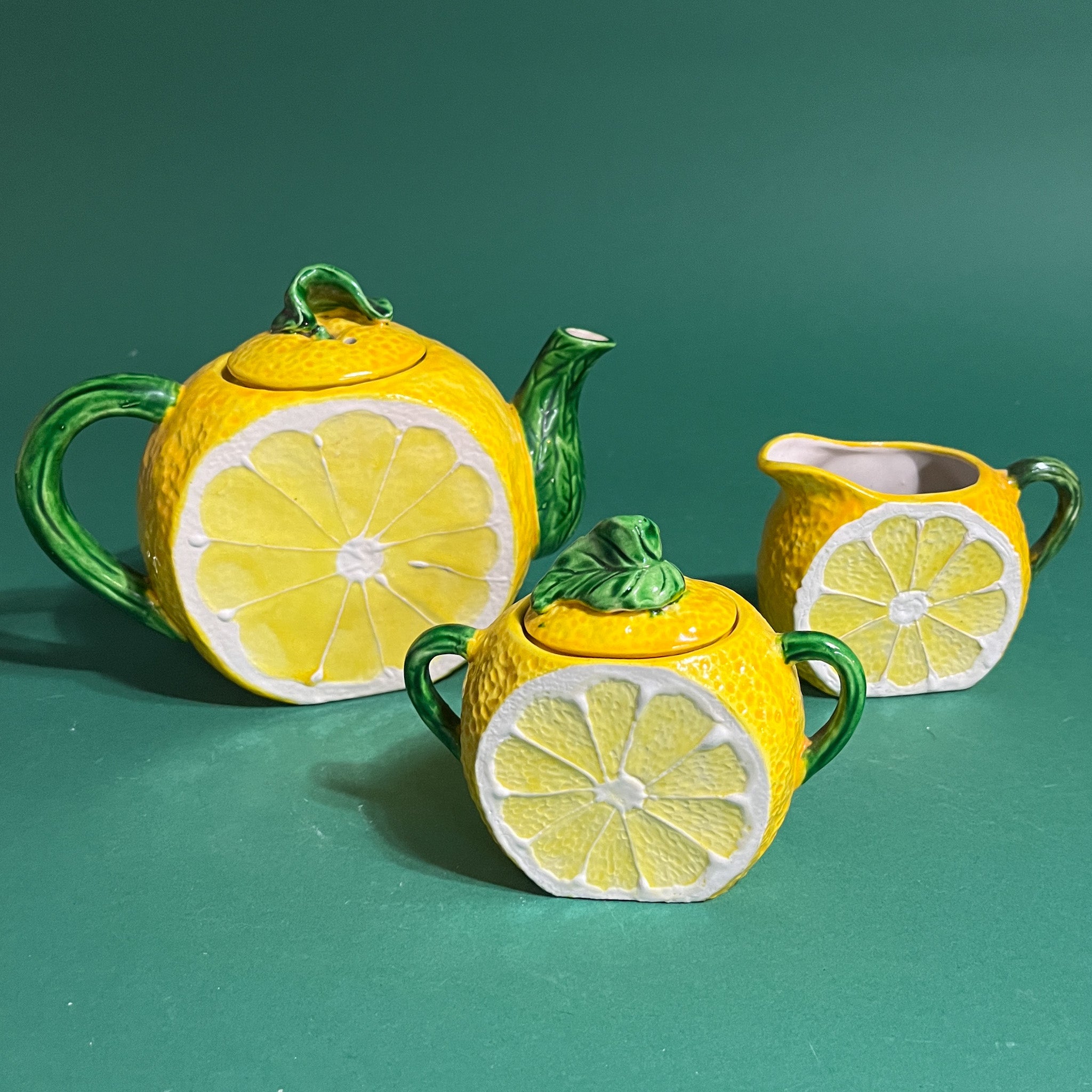 Lemon-themed teapot, sugar bowl, and milk jug set on a green background