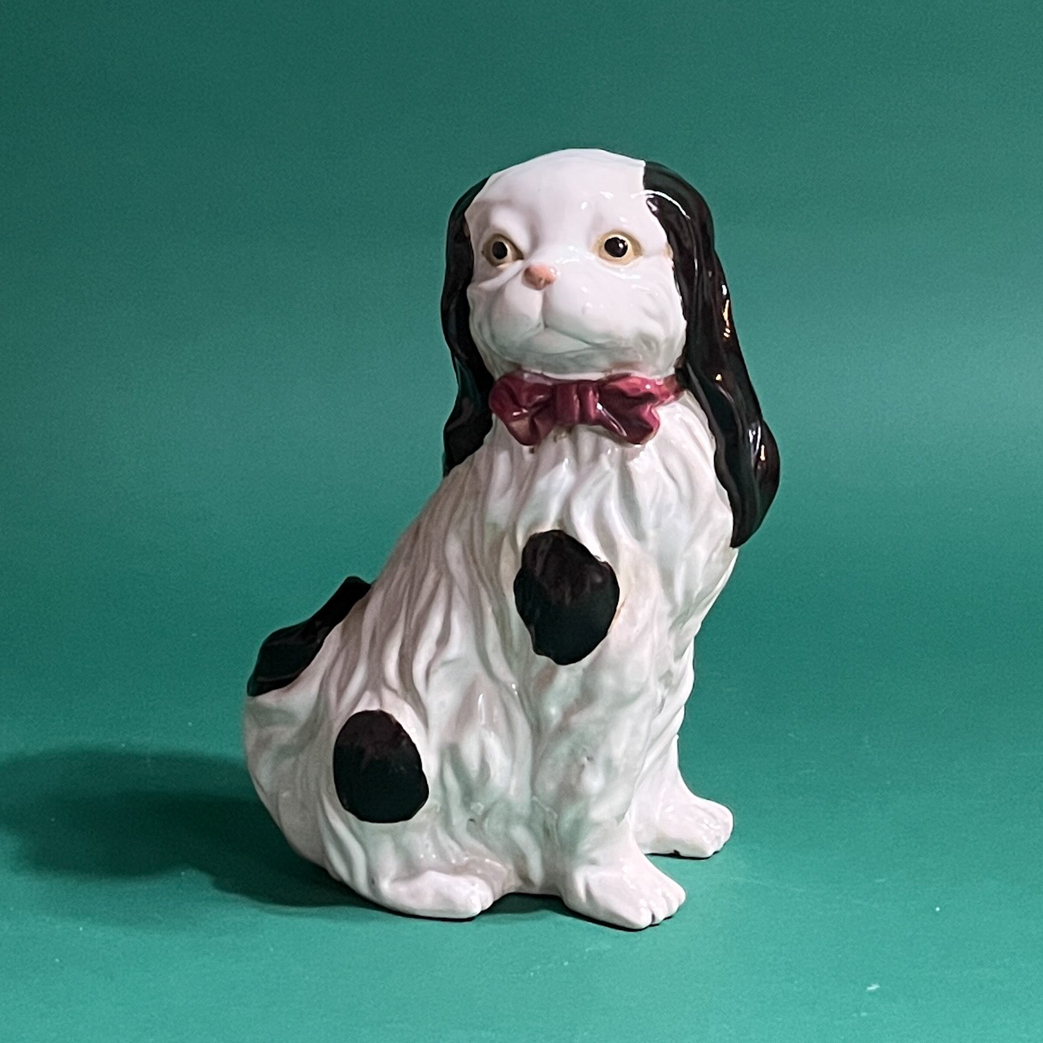 A vintage Staffordshire-style ceramic dog statuette with a black and white coat, red bow tie, and brown details.