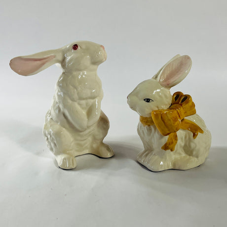 A pair of white vintage ceramic bunnies one with a yellow ribbon on its neck. 