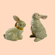 A pair of white vintage ceramic bunnies one with a yellow ribbon on its neck. 