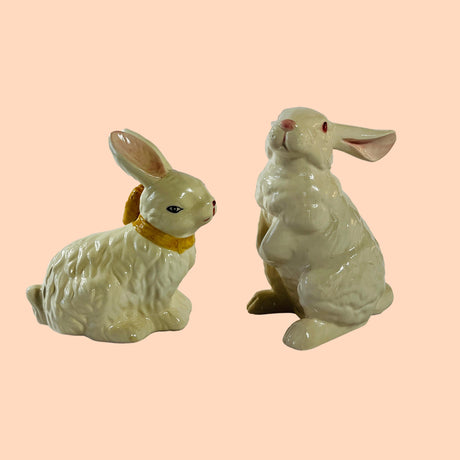 A pair of white vintage ceramic bunnies one with a yellow ribbon on its neck. 