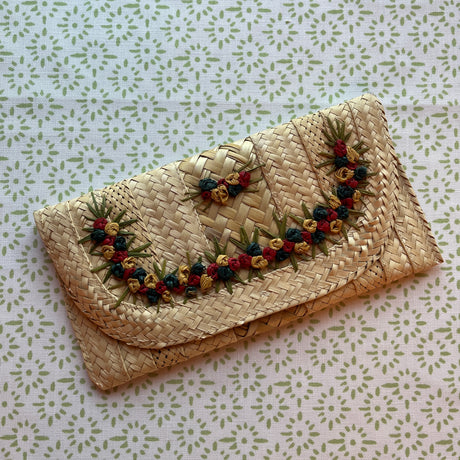 a vintage straw clutch bag with yellow and red flowers around the front