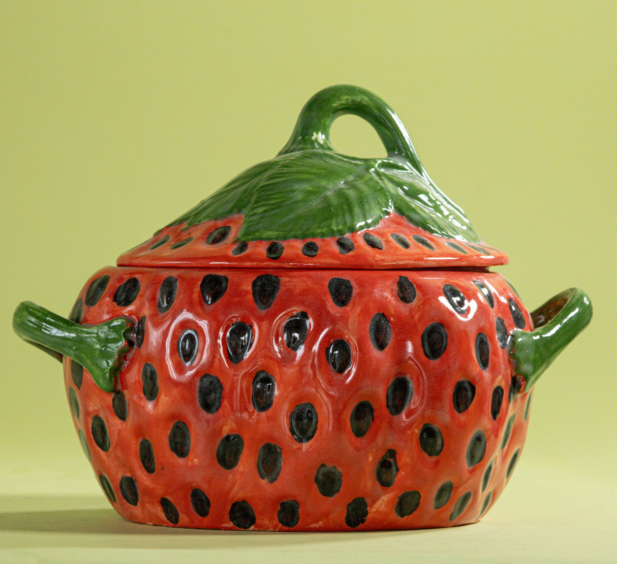 a large red vintage strawberry dish with a green handles and green detail on lid