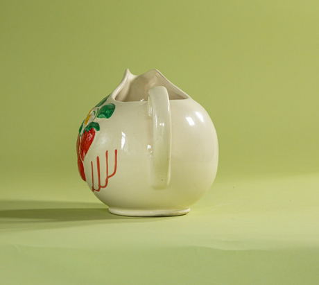 A white vintage strawberry pitcher with strawberry motifs decorating the side