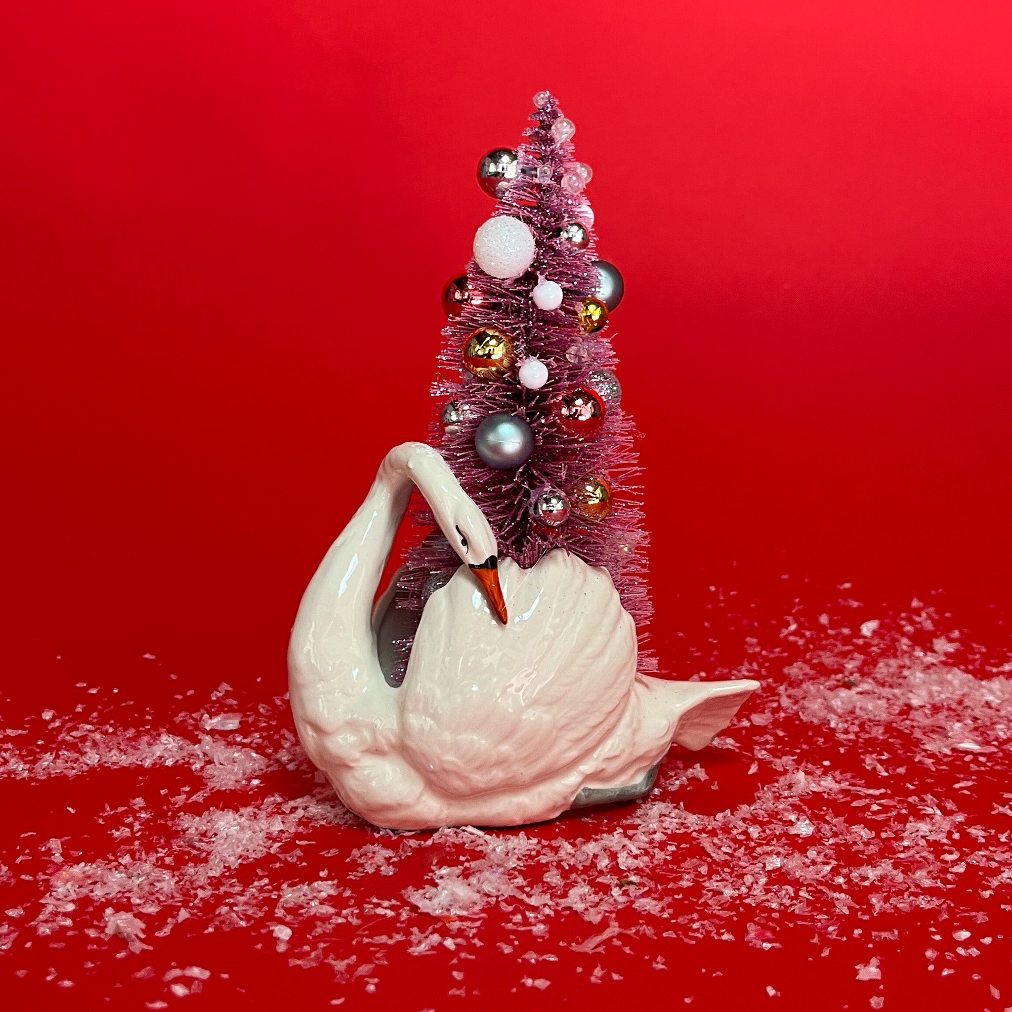 a White Vintage Arched-Neck Ceramic Swan w/Pink Glitter Christmas Tree Centerpiece against a red background. 