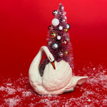 a White Vintage Arched-Neck Ceramic Swan w/Pink Glitter Christmas Tree Centerpiece against a red background. 
