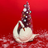 a White Vintage Arched-Neck Ceramic Swan w/Pink Glitter Christmas Tree Centerpiece against a red background. 