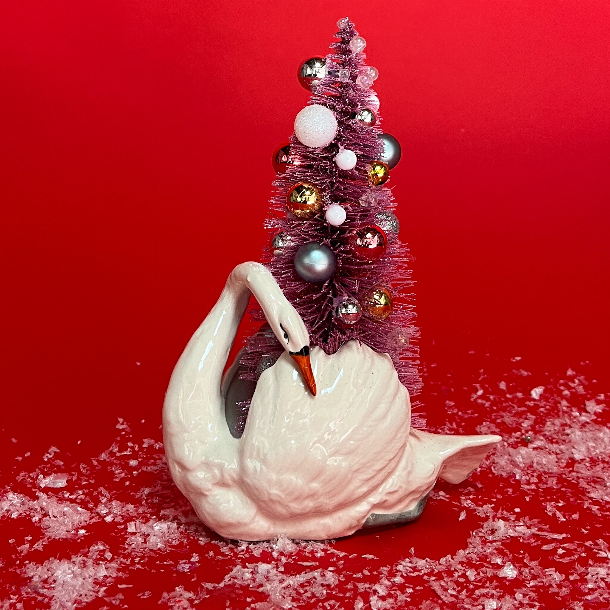 a White Vintage Arched-Neck Ceramic Swan w/Pink Glitter Christmas Tree Centerpiece against a red background. 