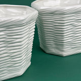 closeup of two white ceramic planters with woven texture on green background