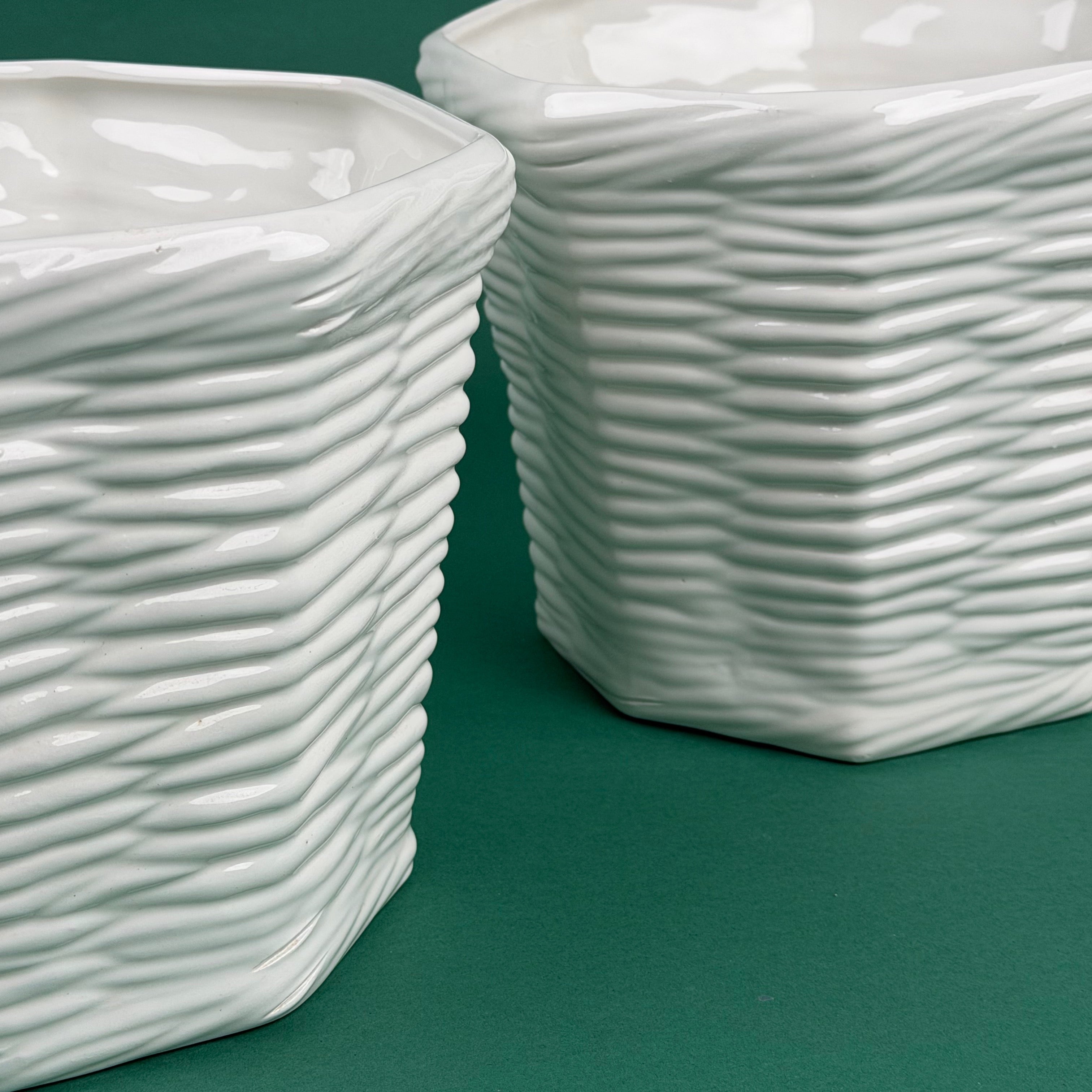 closeup of two white ceramic planters with woven texture on green background