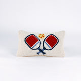 Rectangular white pillow with a hooked wool design of two crossed red and blue pickleball paddles and a yellow pickleball above them.