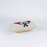 side of a Rectangular white pillow with a hooked wool design of two crossed red and blue pickleball paddles and a yellow pickleball above them.