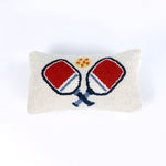 Rectangular white pillow with a hooked wool design of two crossed red and blue pickleball paddles and a yellow pickleball above them.