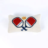 Rectangular white pillow with a hooked wool design of two crossed red and blue pickleball paddles and a yellow pickleball above them.