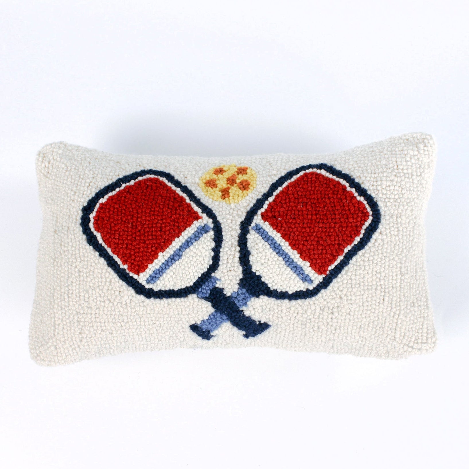 Rectangular white pillow with a hooked wool design of two crossed red and blue pickleball paddles and a yellow pickleball above them.