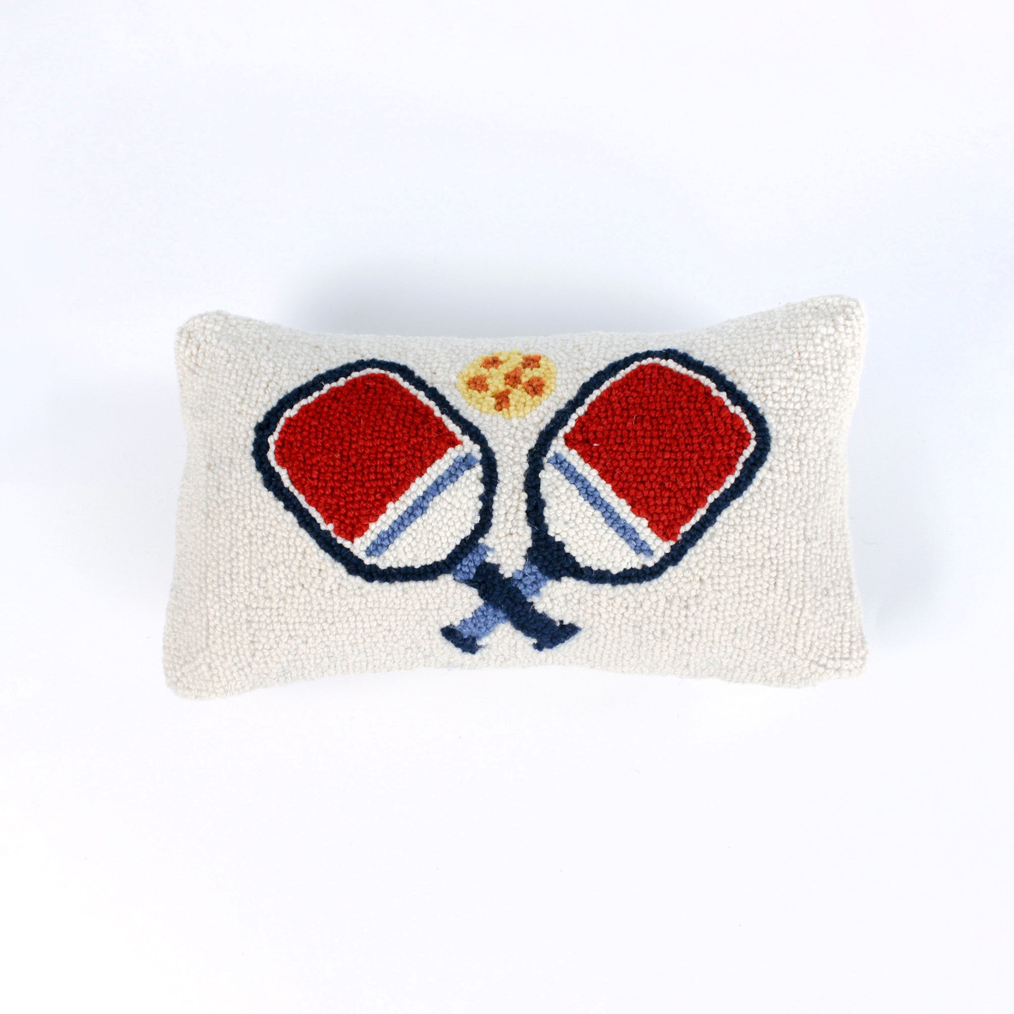 Rectangular white pillow with a hooked wool design of two crossed red and blue pickleball paddles and a yellow pickleball above them.