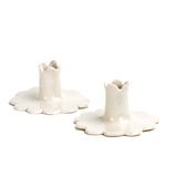 Pair of white ceramic candle holders with scalloped bases and fluted candle cups, photographed on a white background.