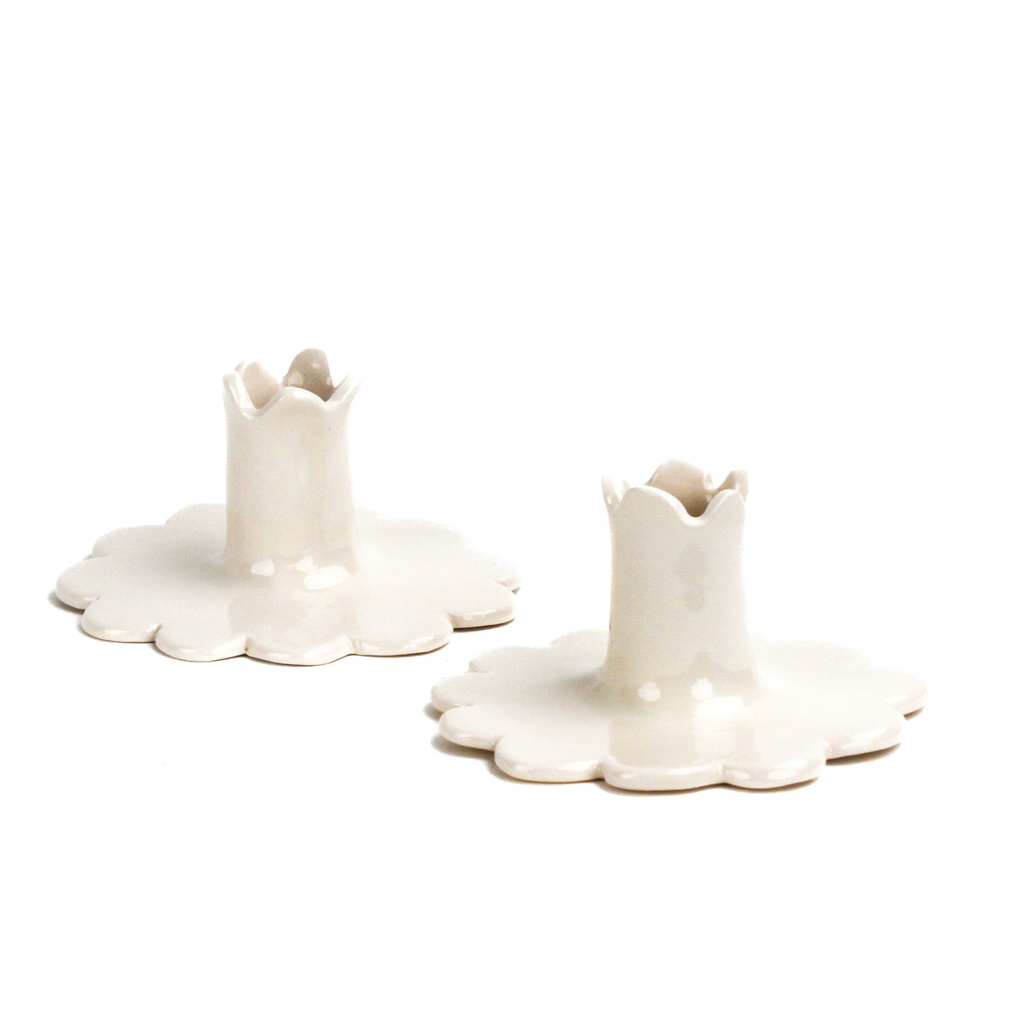 Pair of white ceramic candle holders with scalloped bases and fluted candle cups, photographed on a white background.