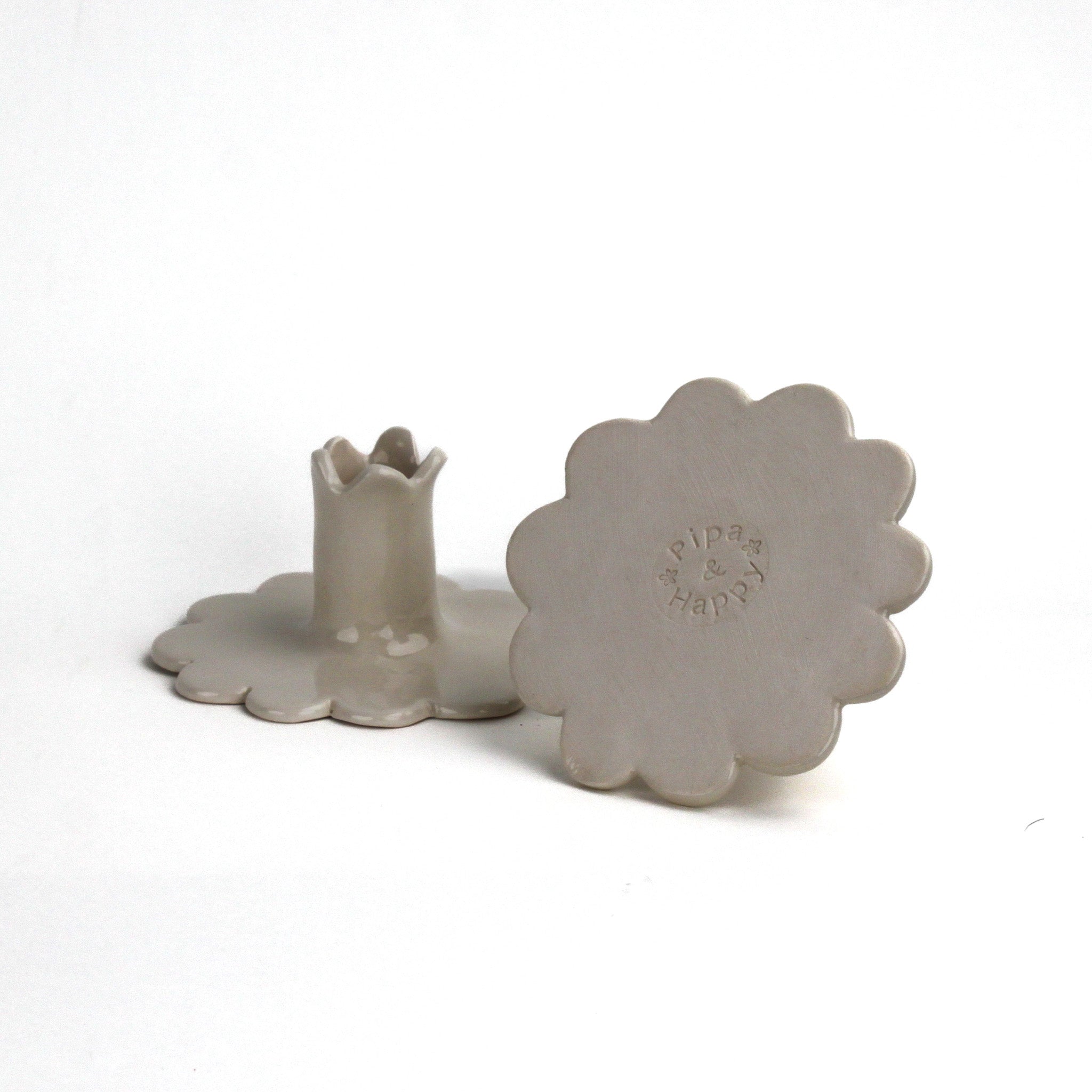 Back and bottom view of two white scalloped ceramic candle holders showing the maker’s mark.