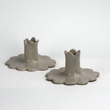“Set of two white scalloped ceramic candle holders with flower-shaped bases.