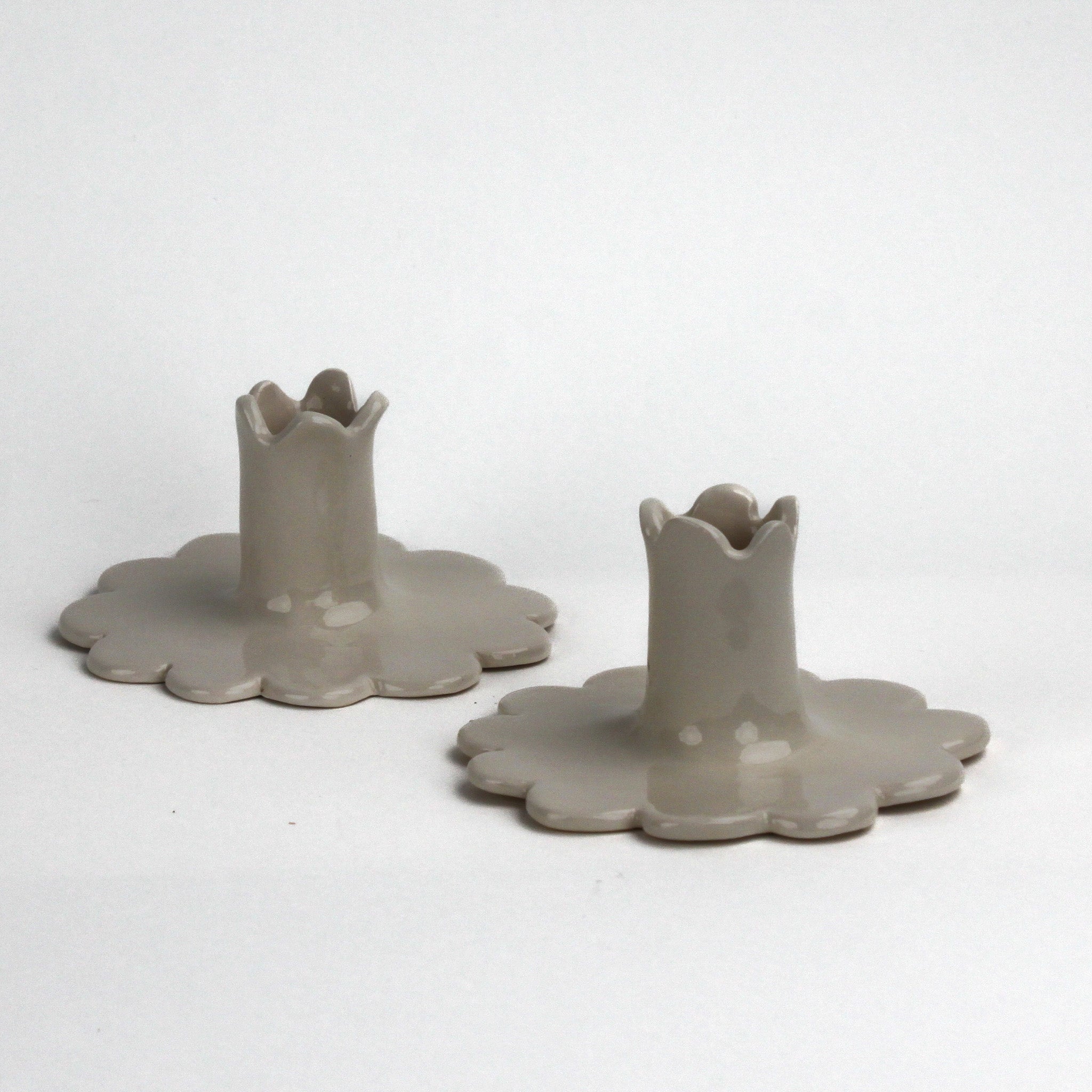 “Set of two white scalloped ceramic candle holders with flower-shaped bases.