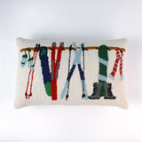 Rectangular white pillow with a hooked wool design featuring colorful skis, poles, boots, and scarves hanging on a wooden rack, evoking a cozy winter ski lodge feel.