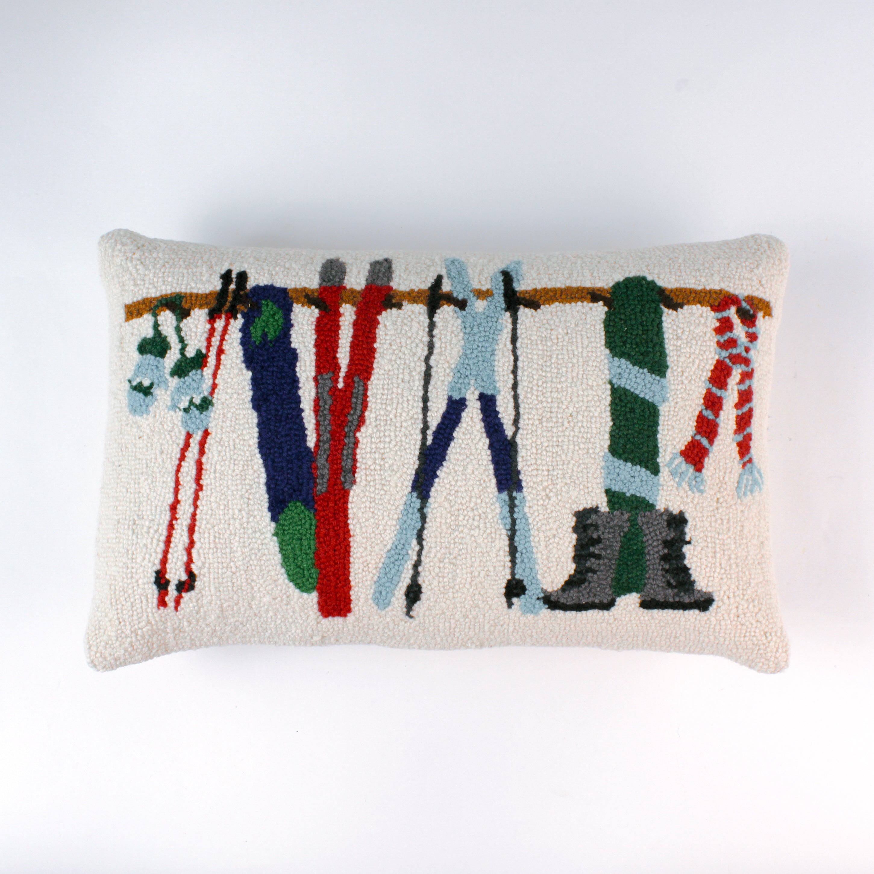 Rectangular white pillow with a hooked wool design featuring colorful skis, poles, boots, and scarves hanging on a wooden rack, evoking a cozy winter ski lodge feel.