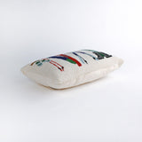 side of a Rectangular white pillow with a hooked wool design featuring colorful skis, poles, boots, and scarves hanging on a wooden rack, evoking a cozy winter ski lodge feel.