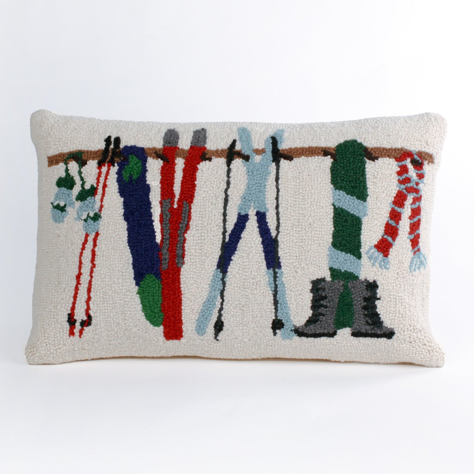 Rectangular white pillow with a hooked wool design featuring colorful skis, poles, boots, and scarves hanging on a wooden rack, evoking a cozy winter ski lodge feel.