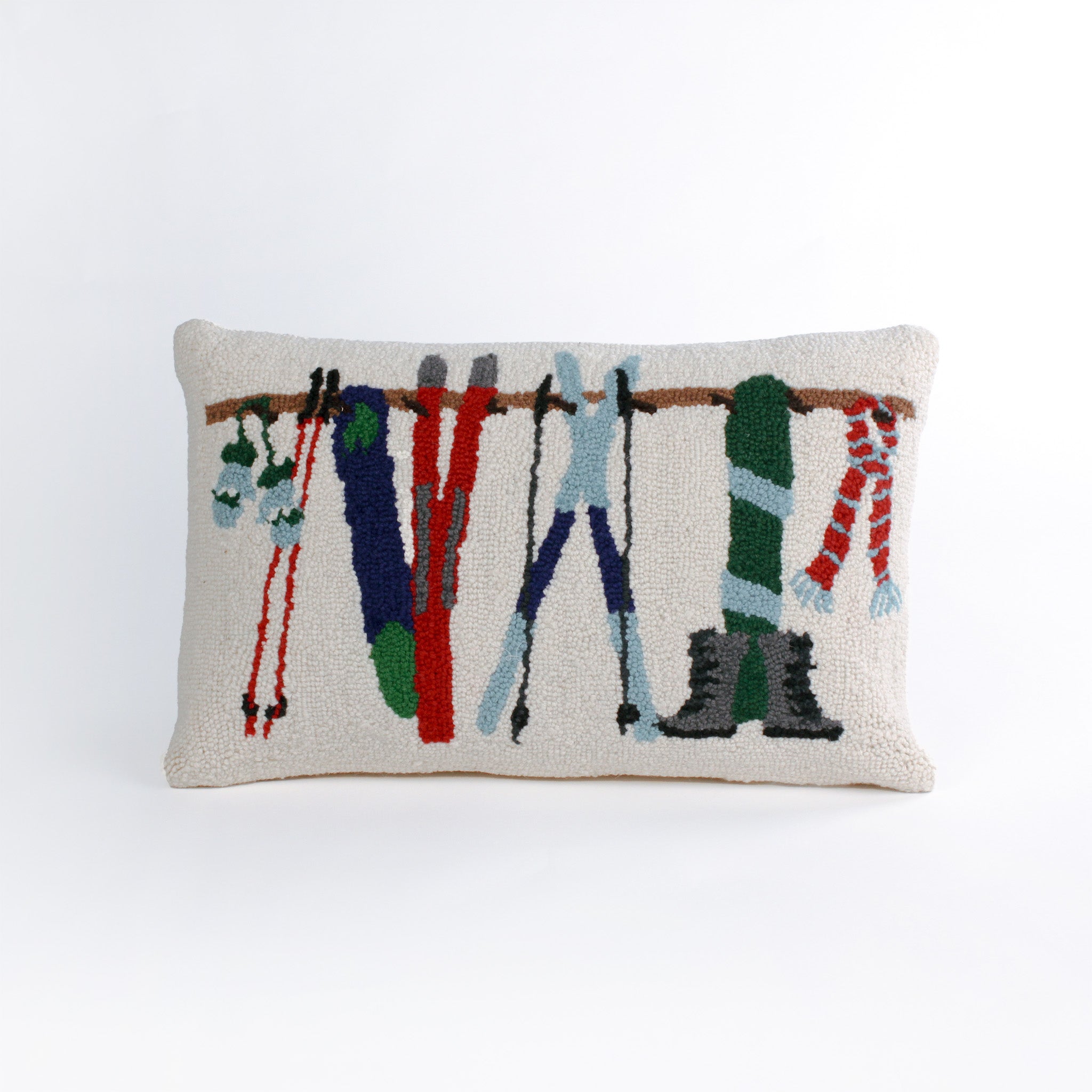 Rectangular white pillow with a hooked wool design featuring colorful skis, poles, boots, and scarves hanging on a wooden rack, evoking a cozy winter ski lodge feel.