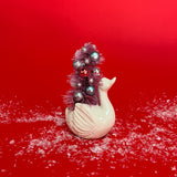 a Vintage Small White Ceramic Swan w/ Pink Glitter Christmas Tree Centerpiece against a red background. 