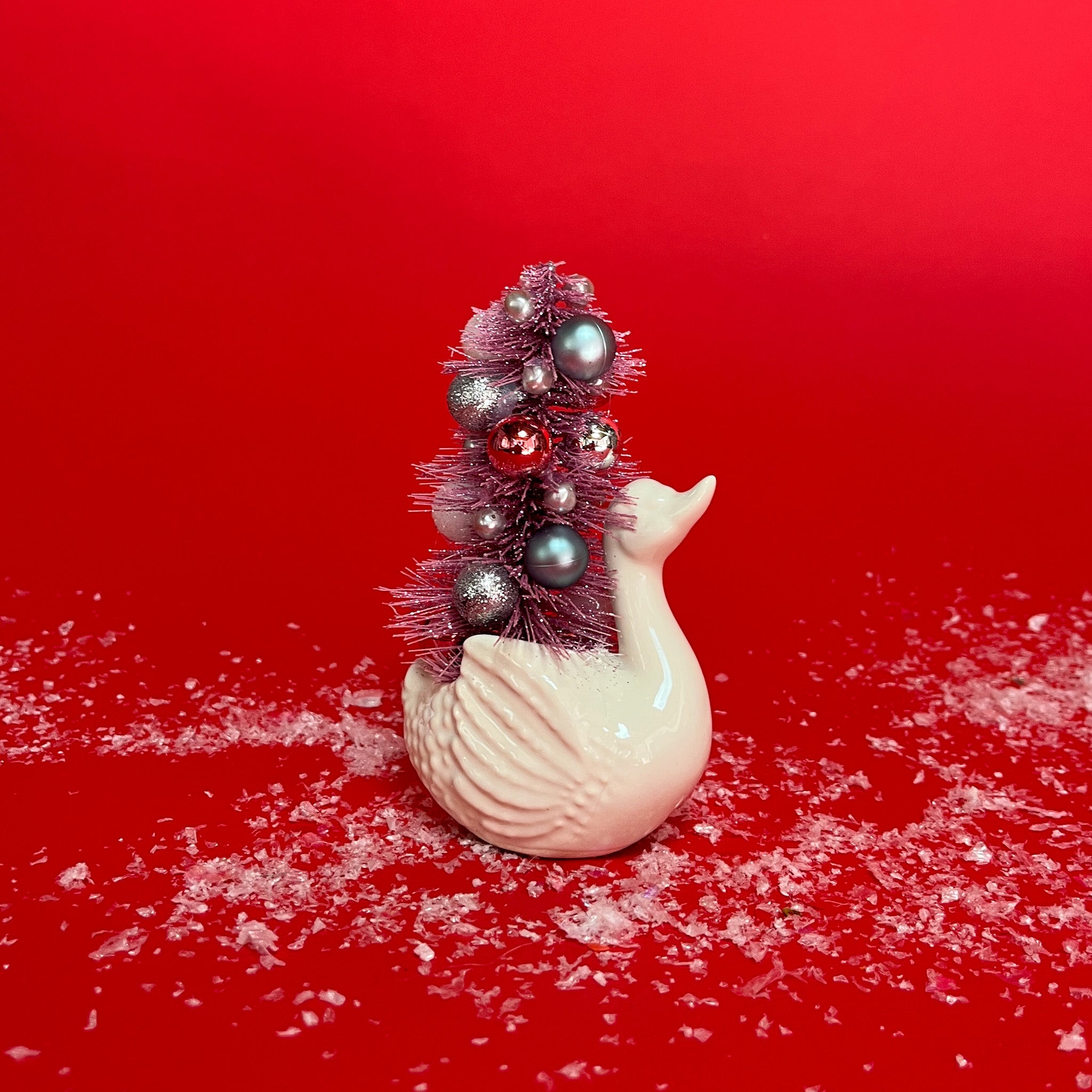 a Vintage Small White Ceramic Swan w/ Pink Glitter Christmas Tree Centerpiece against a red background. 