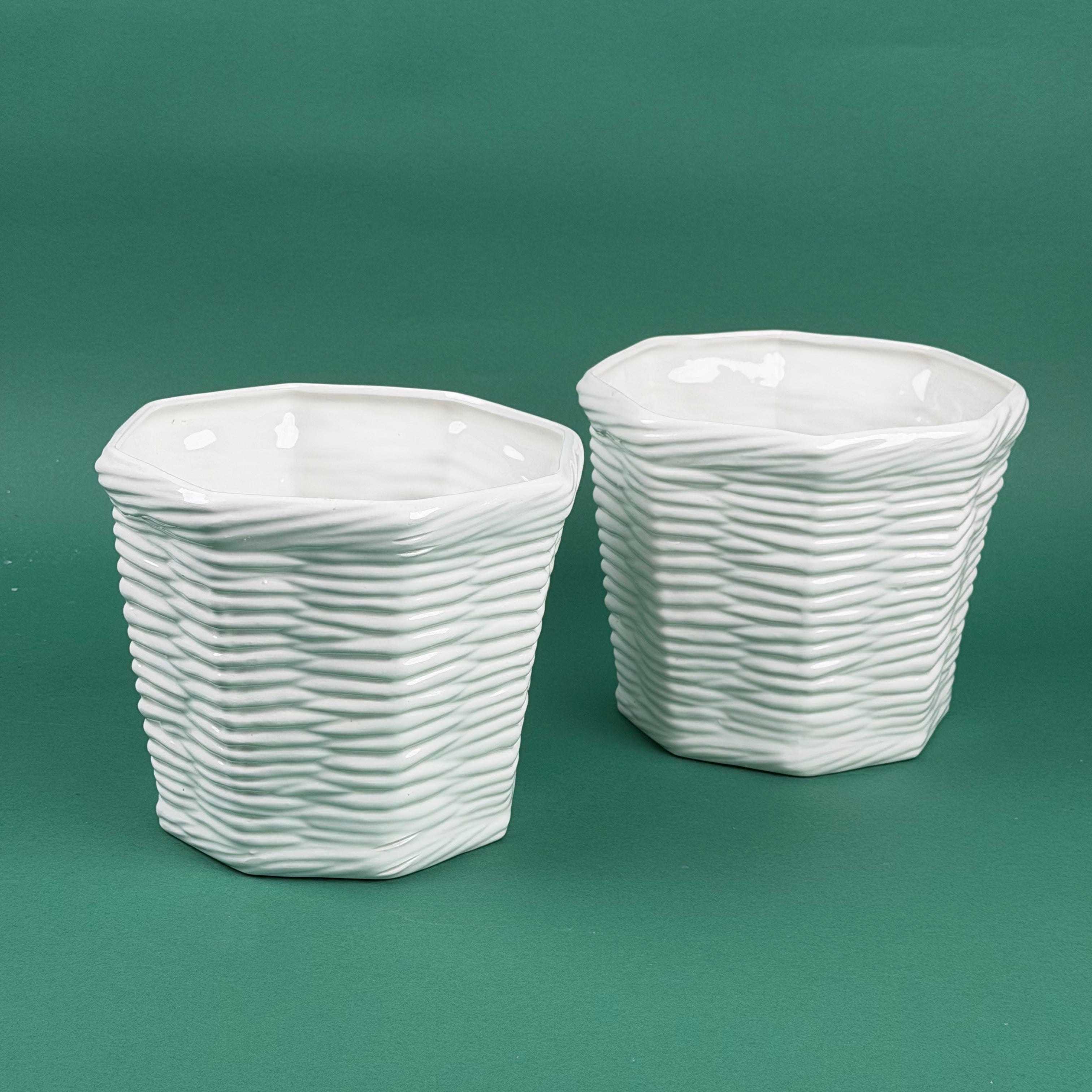 Two white textured ceramic planters with a woven-style design sitting on a green background.