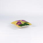 side of a Square decorative pillow with a yellow background featuring a hooked wool design of three purple pansy flowers with green stems and leaves.
