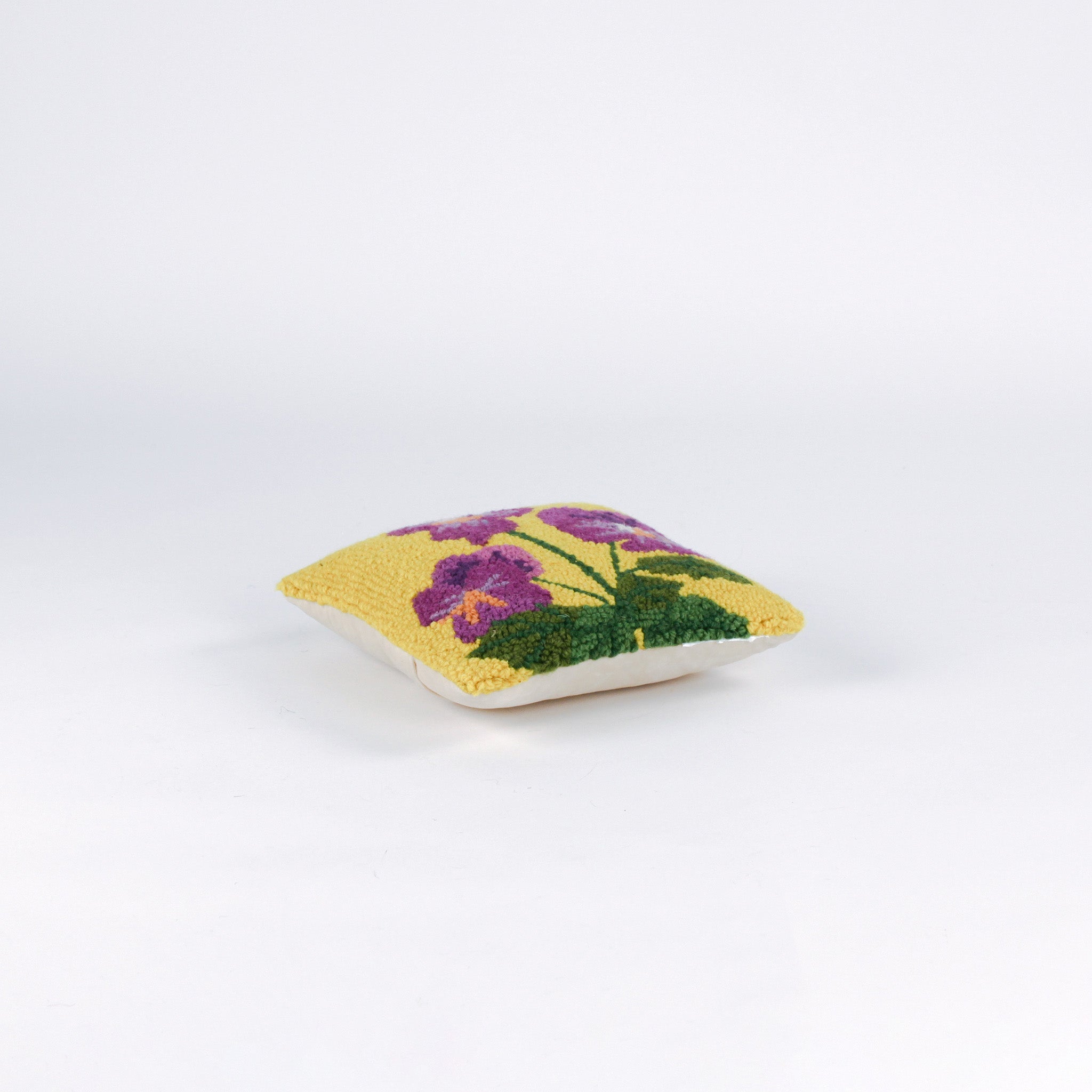 side of a Square decorative pillow with a yellow background featuring a hooked wool design of three purple pansy flowers with green stems and leaves.