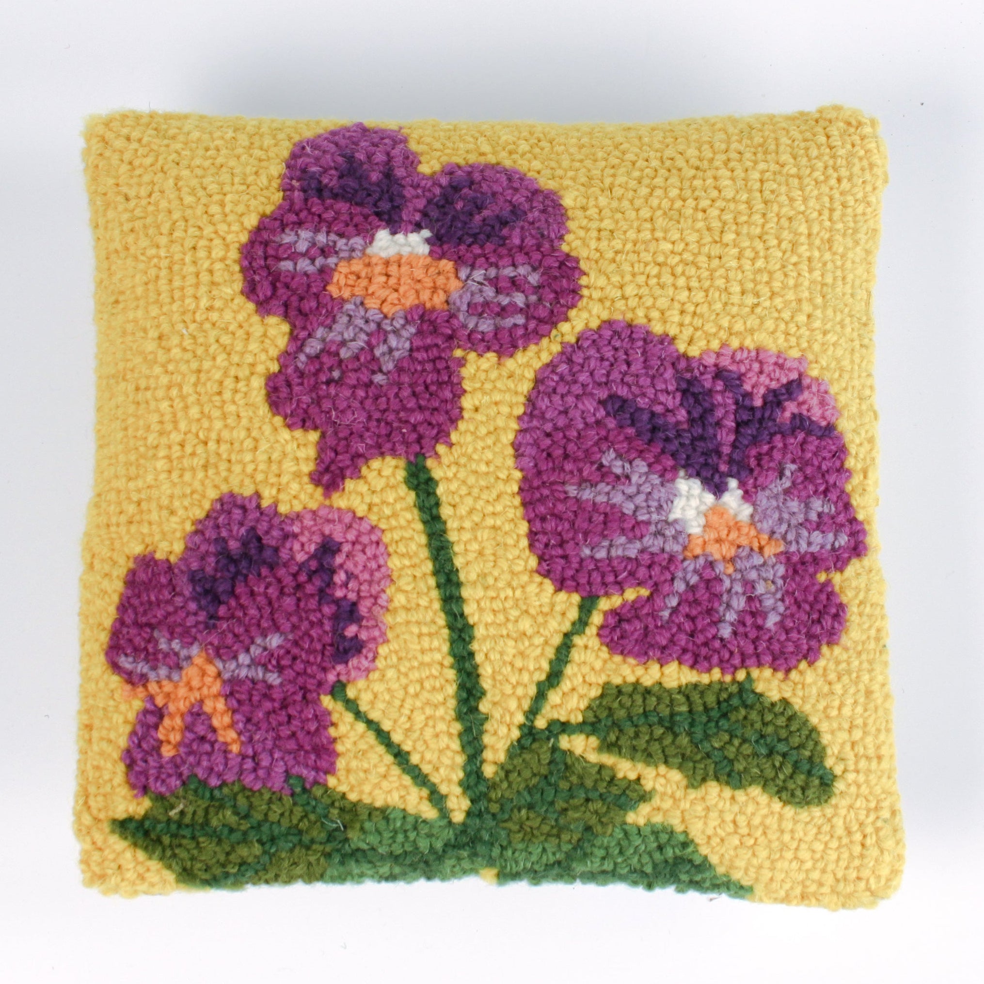 Square decorative pillow with a yellow background featuring a hooked wool design of three purple pansy flowers with green stems and leaves.