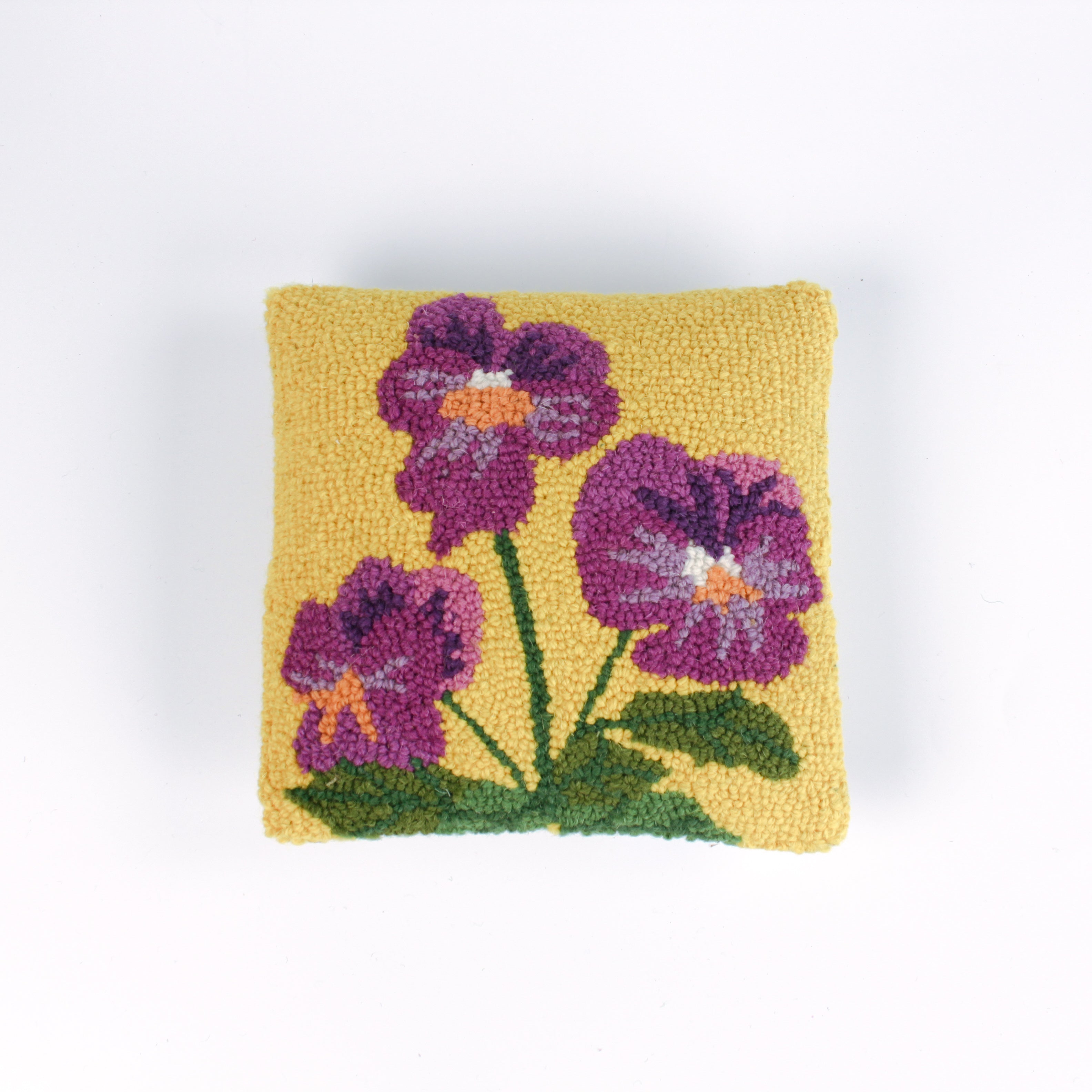Square decorative pillow with a yellow background featuring a hooked wool design of three purple pansy flowers with green stems and leaves.