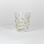 Clear glass tumbler with gold polka dots on a white background