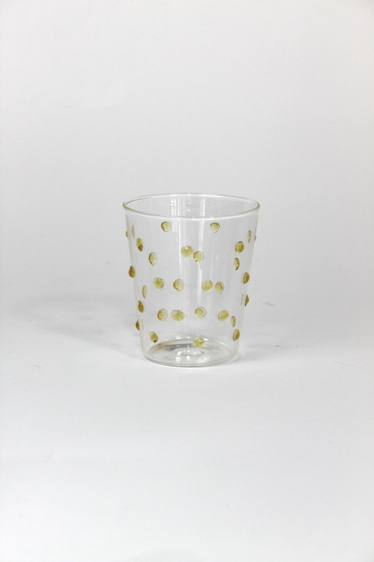 Clear glass tumbler with gold polka dots on a white background